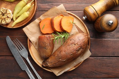 Photo of Tasty cooked sweet potatoes served with rosemary on wooden table, top view