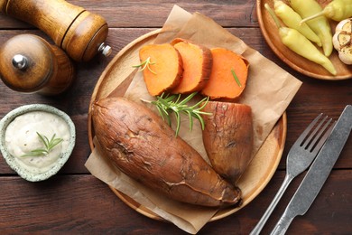 Photo of Tasty cooked sweet potatoes served with rosemary and sauce on wooden table, top view