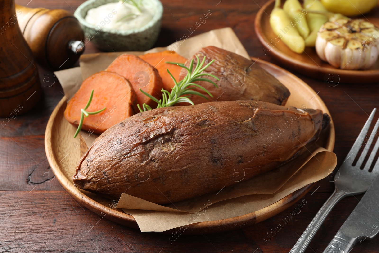 Photo of Tasty cooked sweet potatoes served with rosemary on wooden table, closeup