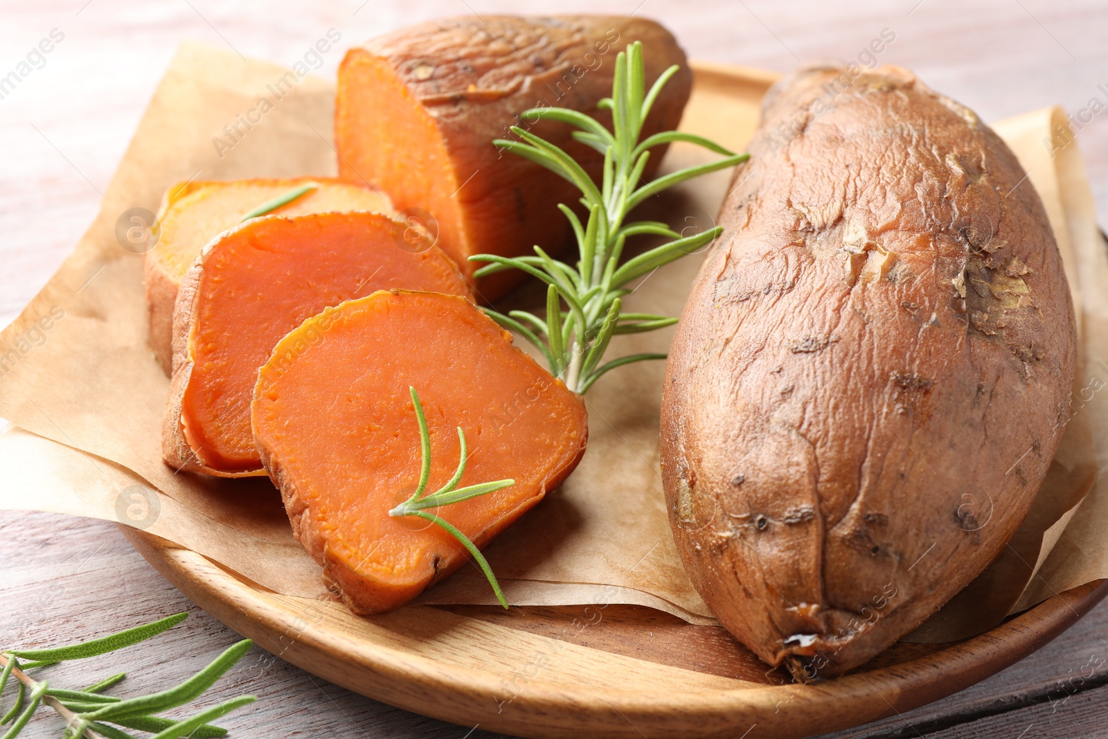 Photo of Tasty cooked sweet potatoes and rosemary on wooden table, closeup