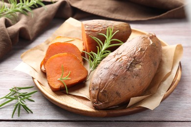 Photo of Tasty cooked sweet potatoes and rosemary on wooden table, closeup