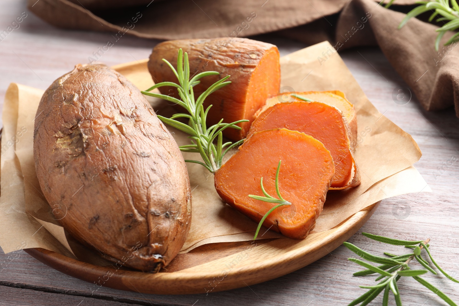 Photo of Tasty cooked sweet potatoes and rosemary on wooden table, closeup