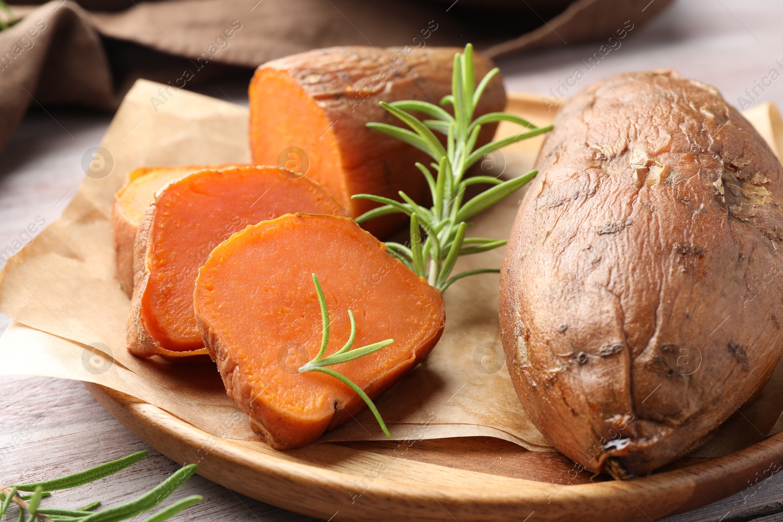 Photo of Tasty cooked sweet potatoes and rosemary on wooden table, closeup