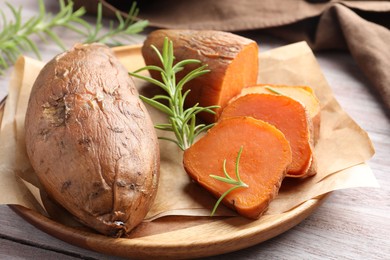 Photo of Tasty cooked sweet potatoes and rosemary on wooden table, closeup