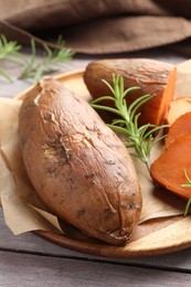 Photo of Tasty cooked sweet potatoes and rosemary on wooden table, closeup