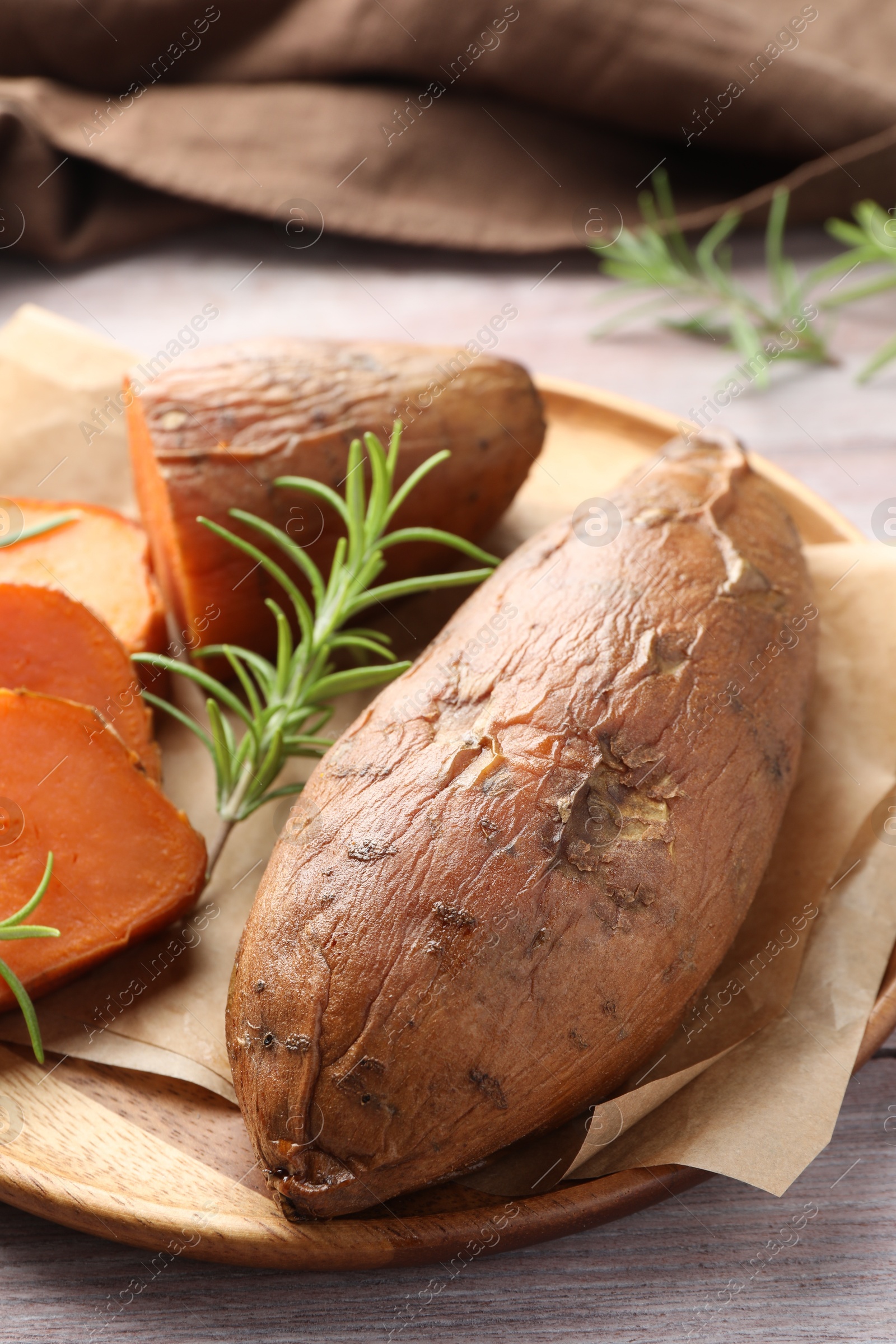 Photo of Tasty cooked sweet potatoes and rosemary on wooden table, closeup