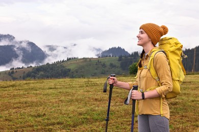 Young hiker with trekking poles and backpack in mountains outdoors, space for text