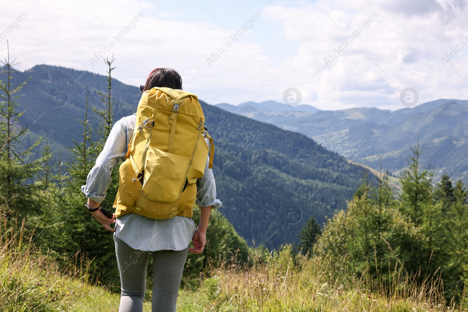 Photo of Young hiker with backpack walking in mountains, back view