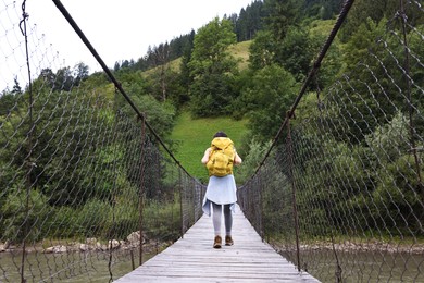 Photo of Young hiker walking on wooden bridge over river, back view