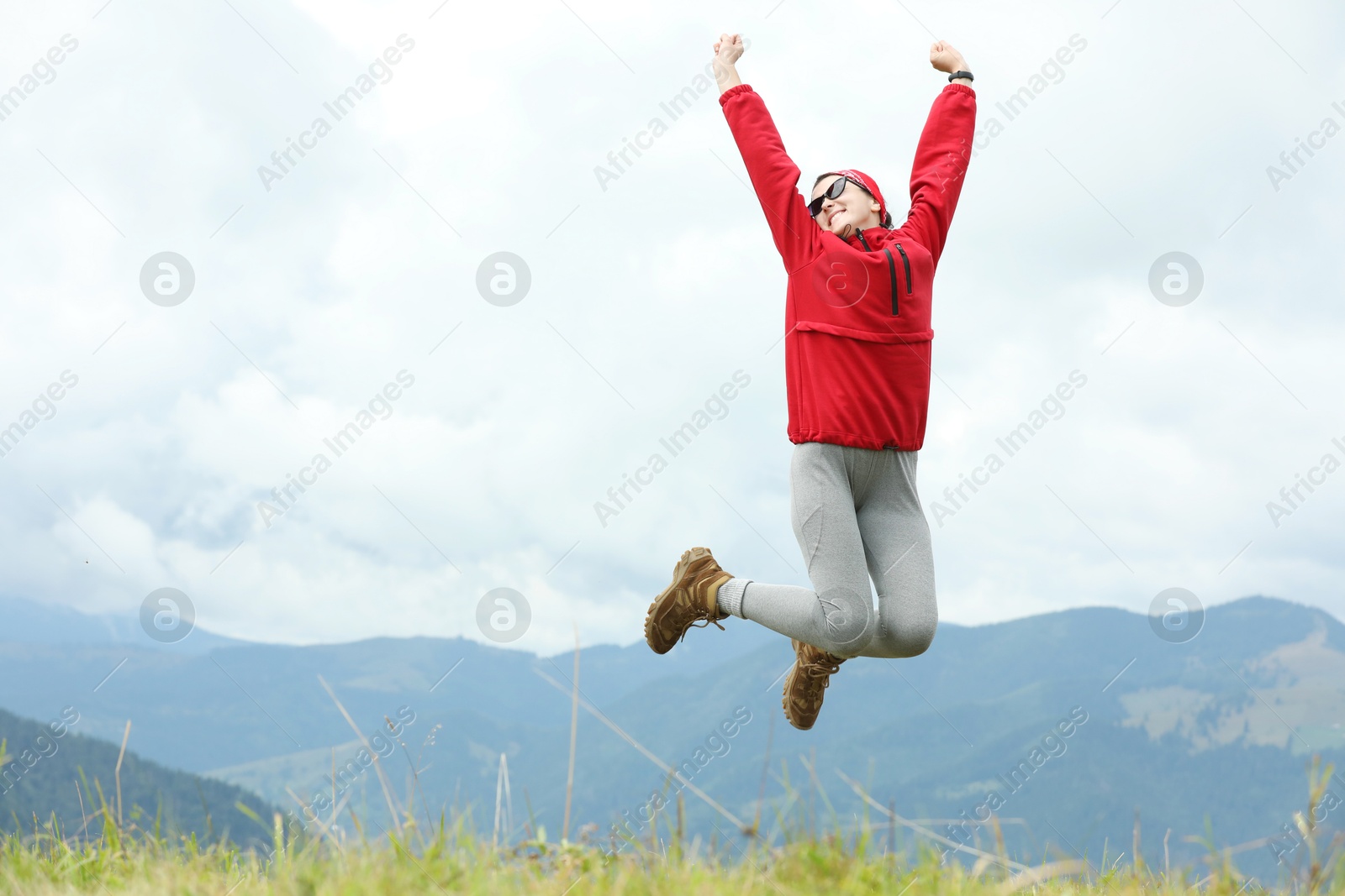 Photo of Happy young hiker jumping in mountains, low angle view. Space for text