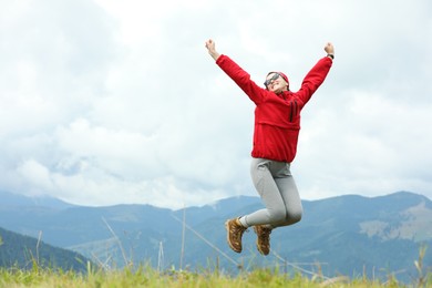 Photo of Happy young hiker jumping in mountains, low angle view. Space for text