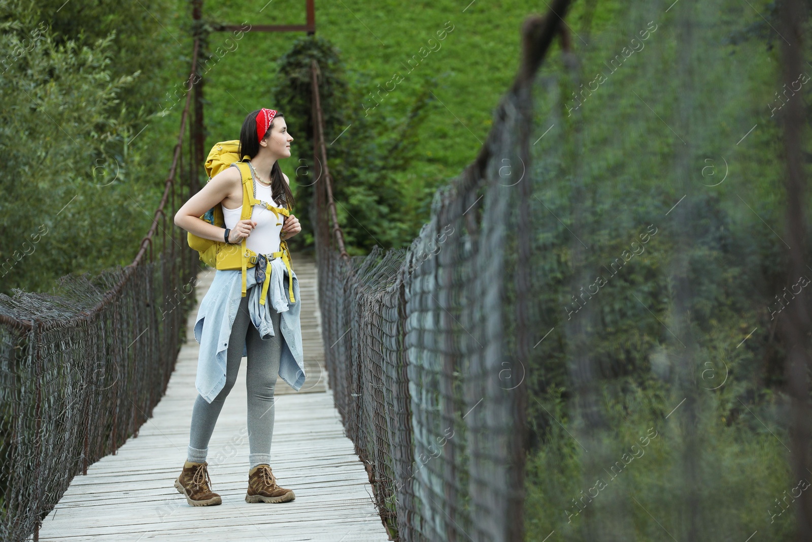 Photo of Young hiker walking on wooden bridge over river