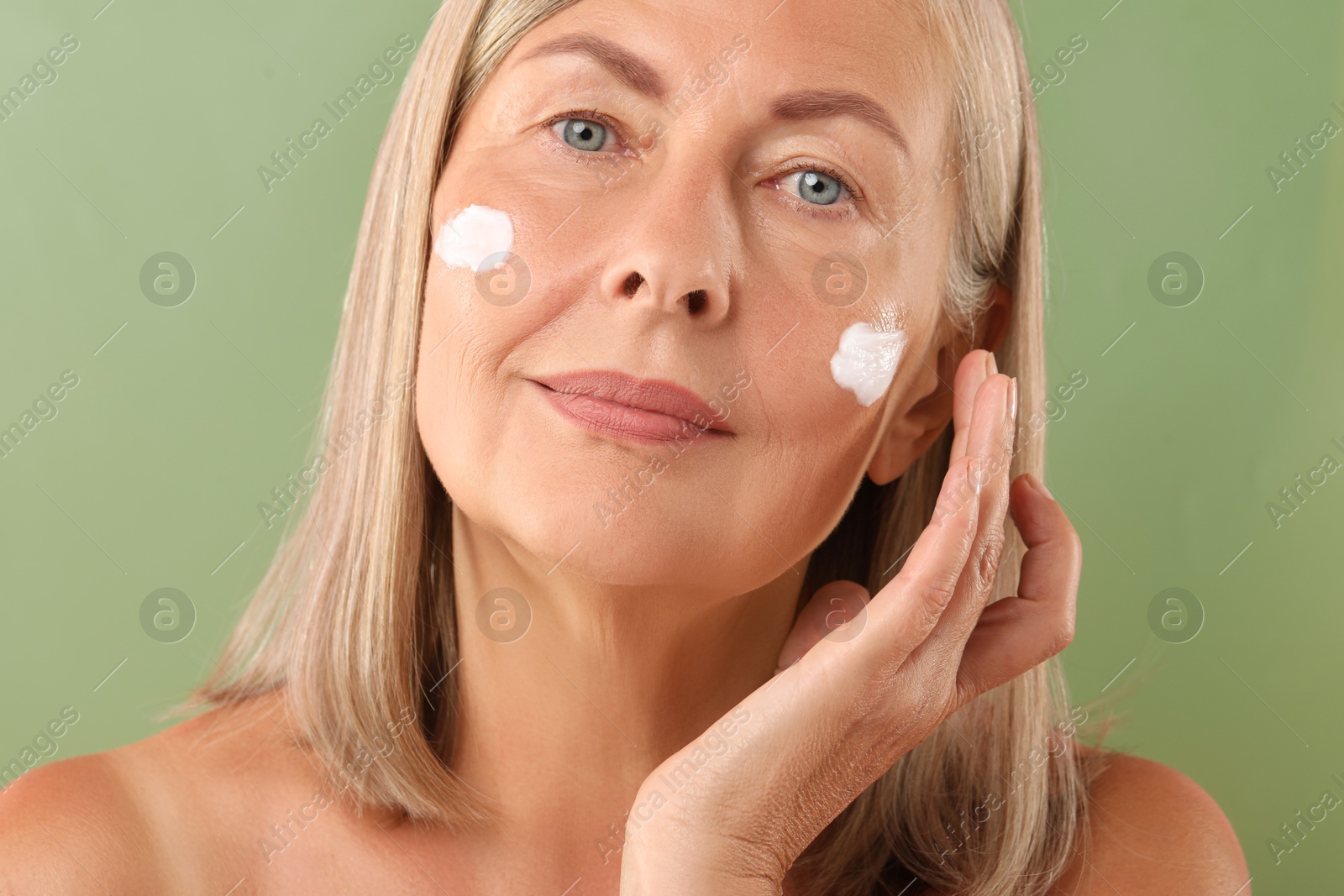 Photo of Senior woman with face cream on green background, closeup