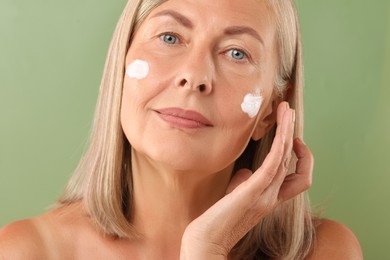 Senior woman with face cream on green background, closeup