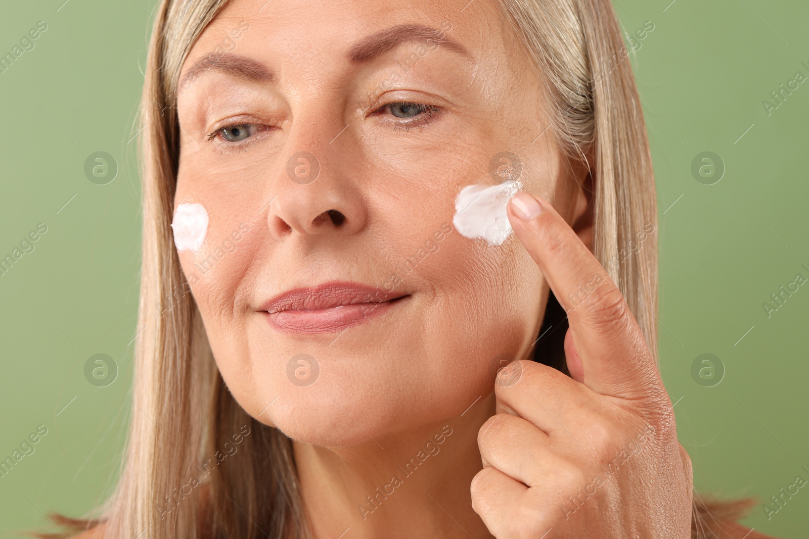 Photo of Senior woman applying face cream on green background, closeup