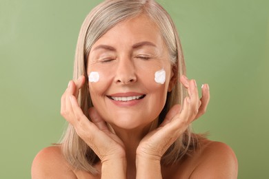 Photo of Senior woman with face cream on green background