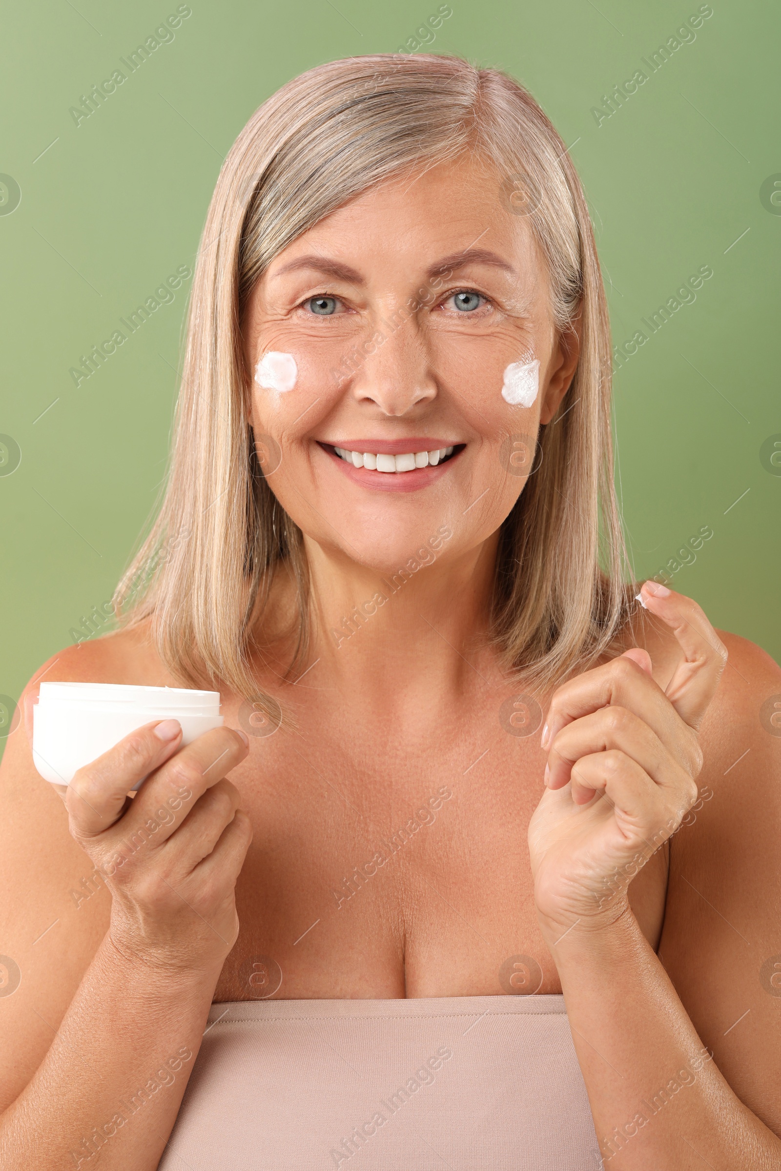 Photo of Senior woman with face cream on green background