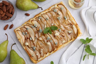 Photo of Delicious puff pastry tart with pears, almond, mint and blue cheese on light table, flat lay