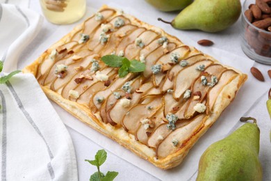 Photo of Delicious puff pastry tart with pears, almond, mint and blue cheese on light table, closeup