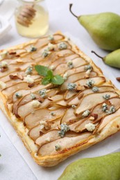 Photo of Delicious puff pastry tart with pears, almond, mint and blue cheese on light table, closeup