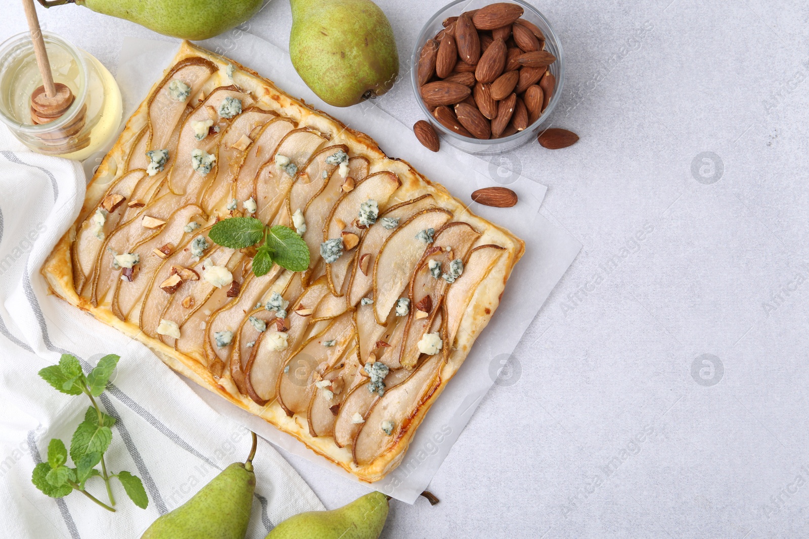 Photo of Delicious puff pastry tart with pears, almond, mint and blue cheese on light table, flat lay. Space for text