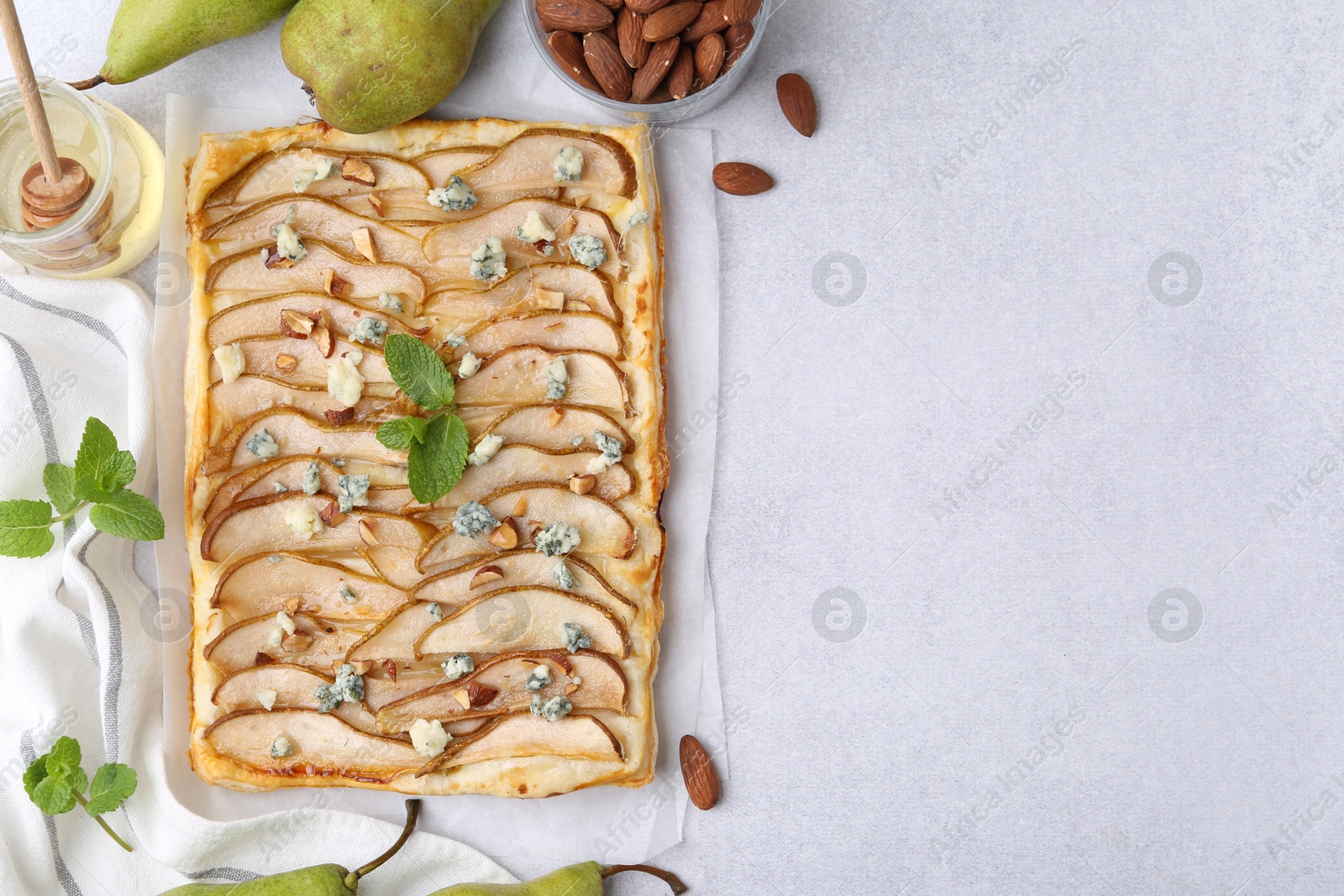 Photo of Delicious puff pastry tart with pears, almond, mint and blue cheese on light table, flat lay. Space for text