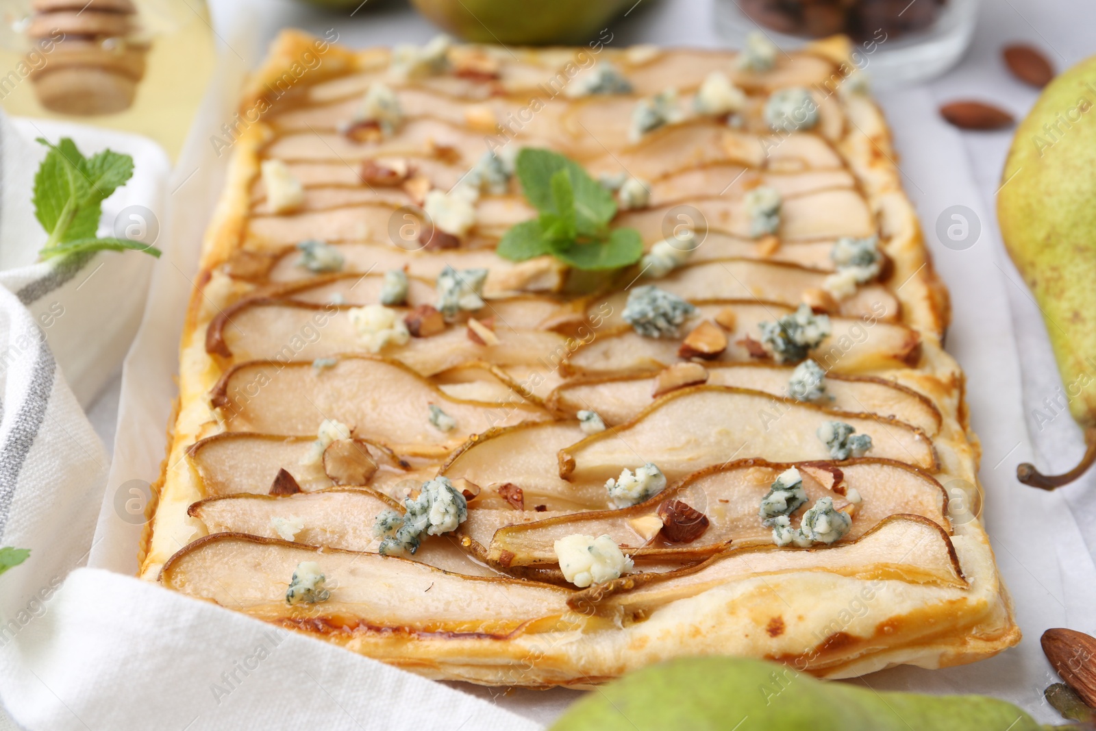 Photo of Delicious puff pastry tart with pears, almond, mint and blue cheese on light table, closeup