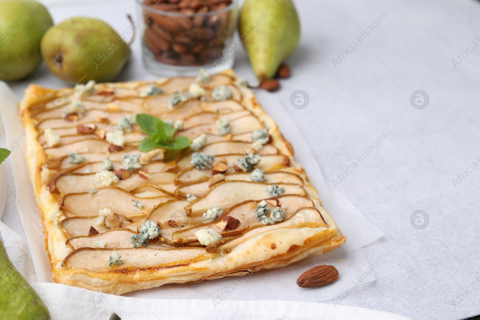 Photo of Delicious puff pastry tart with pears, almond, mint and blue cheese on light table, closeup. Space for text