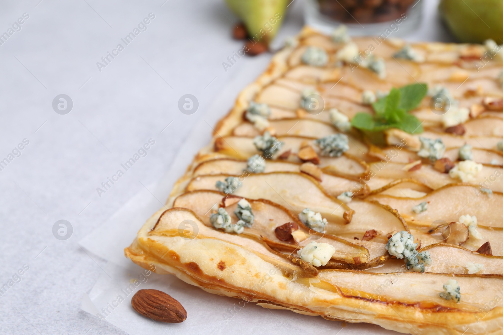 Photo of Delicious puff pastry tart with pears, almond, mint and blue cheese on light table, closeup. Space for text