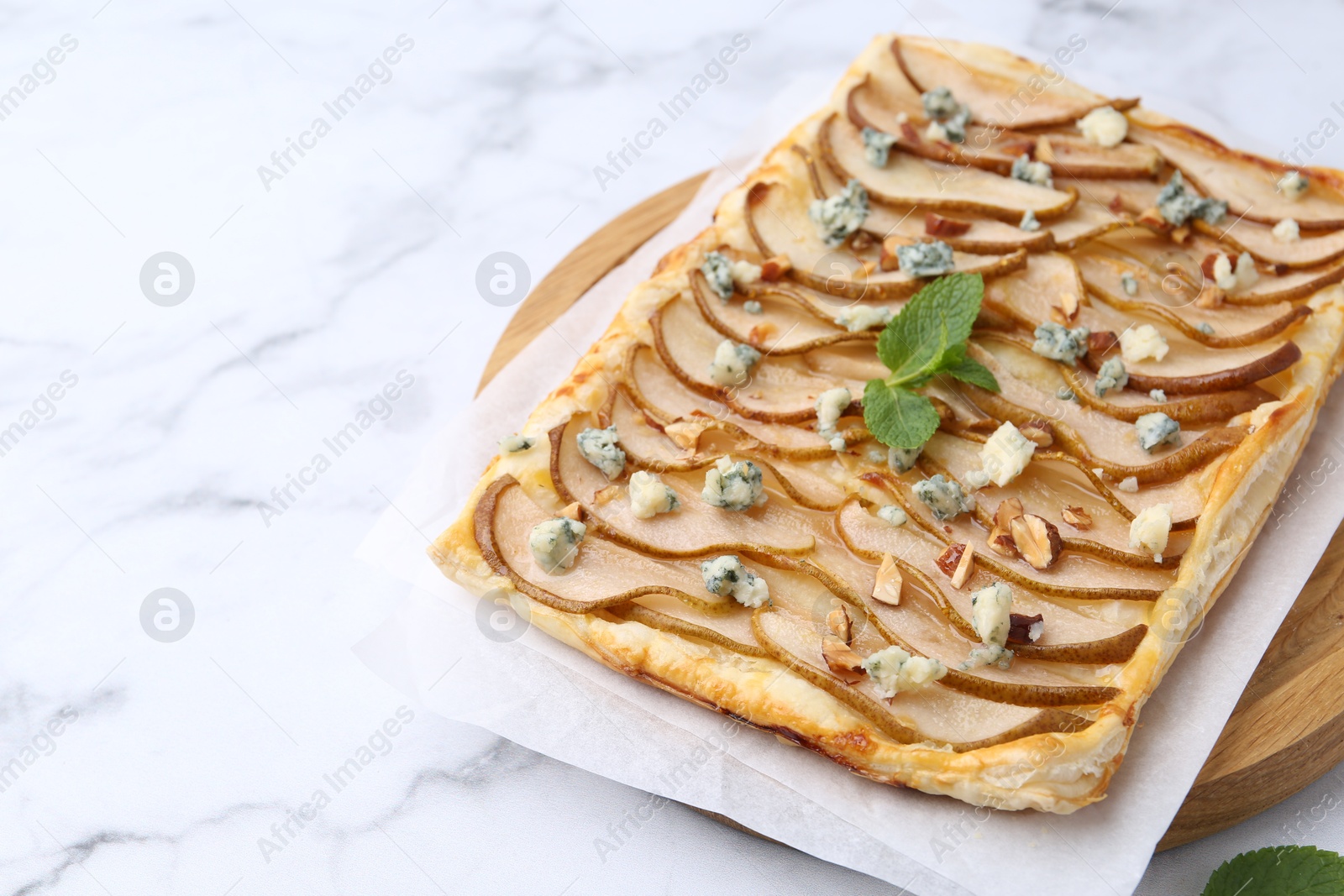 Photo of Delicious puff pastry tart with pears, almond, mint and blue cheese on white marble table, closeup. Space for text