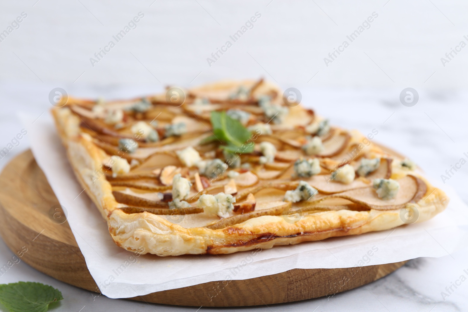 Photo of Delicious puff pastry tart with pears, almond, mint and blue cheese on white table, closeup