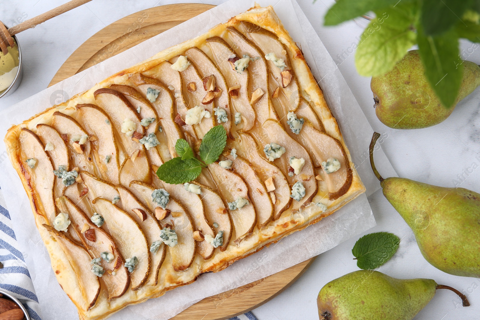 Photo of Delicious puff pastry tart with pears, almond, mint and blue cheese on light table, flat lay