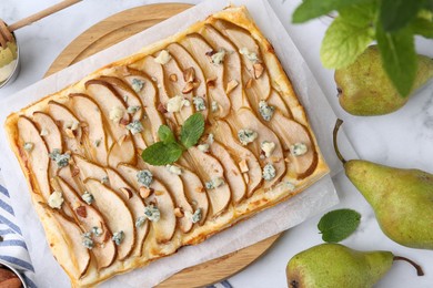 Delicious puff pastry tart with pears, almond, mint and blue cheese on light table, flat lay