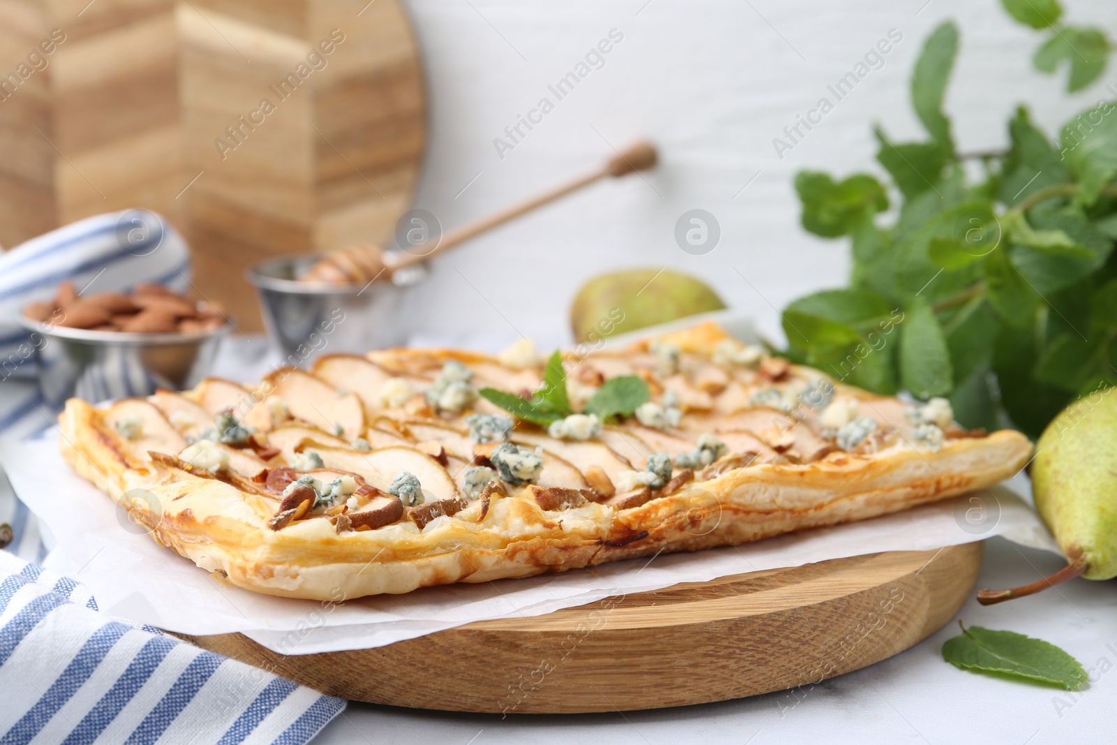 Photo of Delicious puff pastry tart with pears, almond, mint and blue cheese on white table, closeup