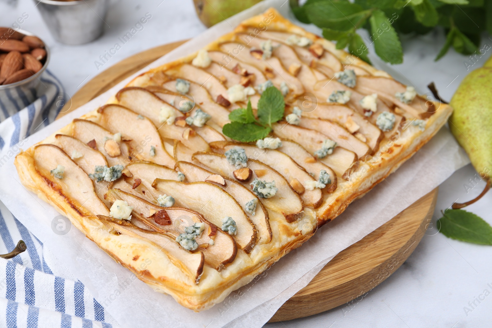 Photo of Delicious puff pastry tart with pears, almond, mint and blue cheese on white table, closeup