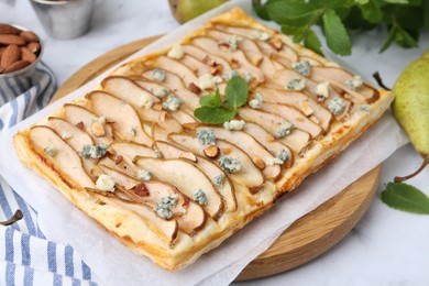 Photo of Delicious puff pastry tart with pears, almond, mint and blue cheese on white table, closeup