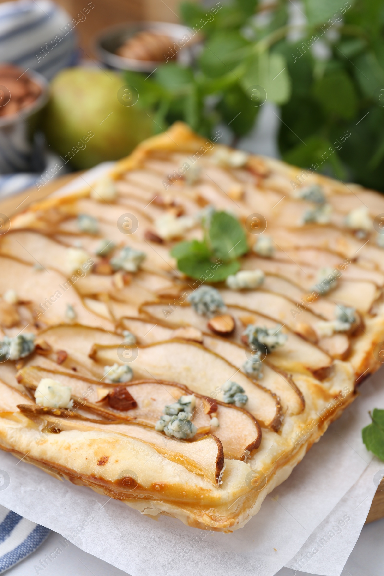 Photo of Delicious puff pastry tart with pears, almond, mint and blue cheese on white table, closeup