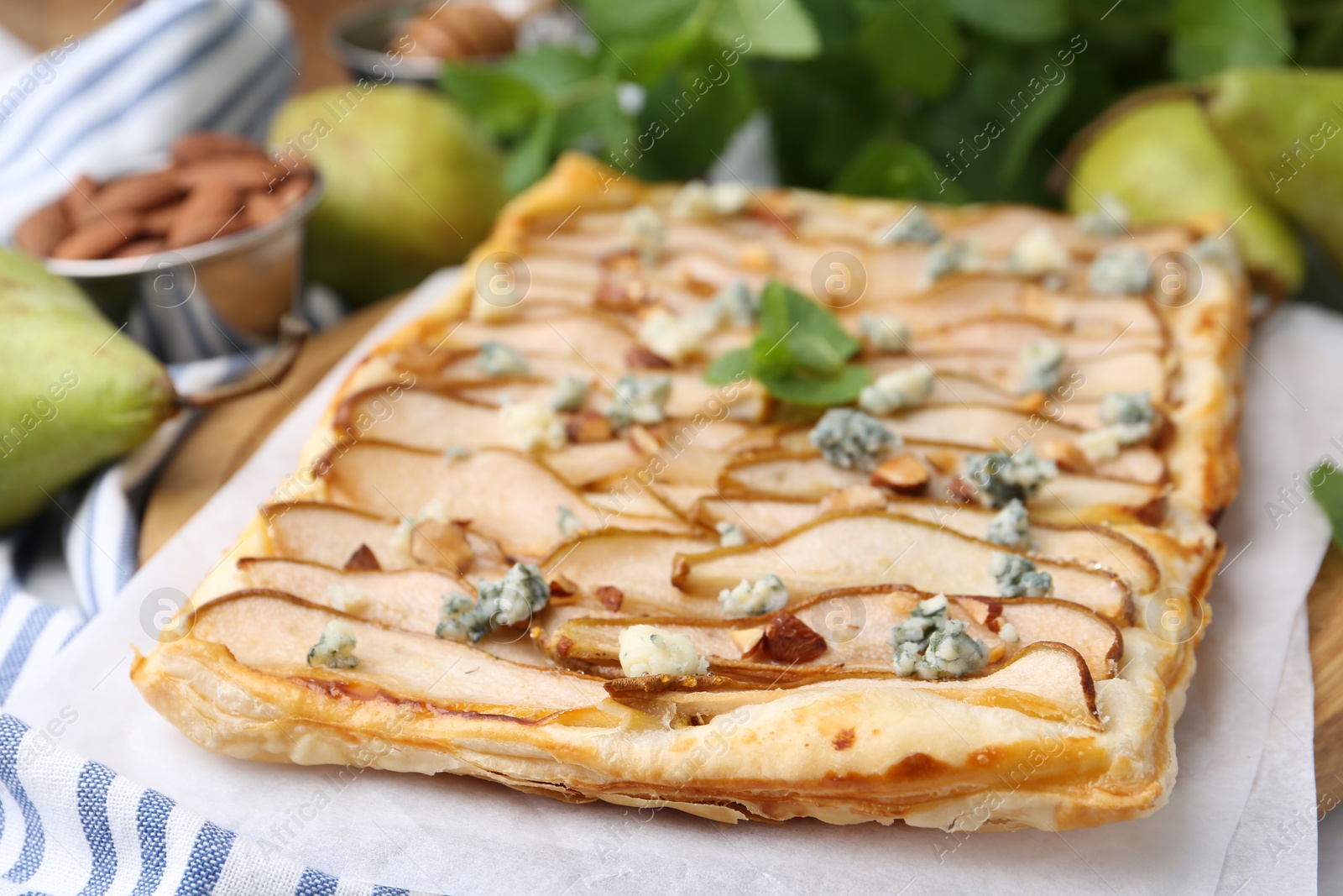 Photo of Delicious puff pastry tart with pears, almond, mint and blue cheese on table, closeup