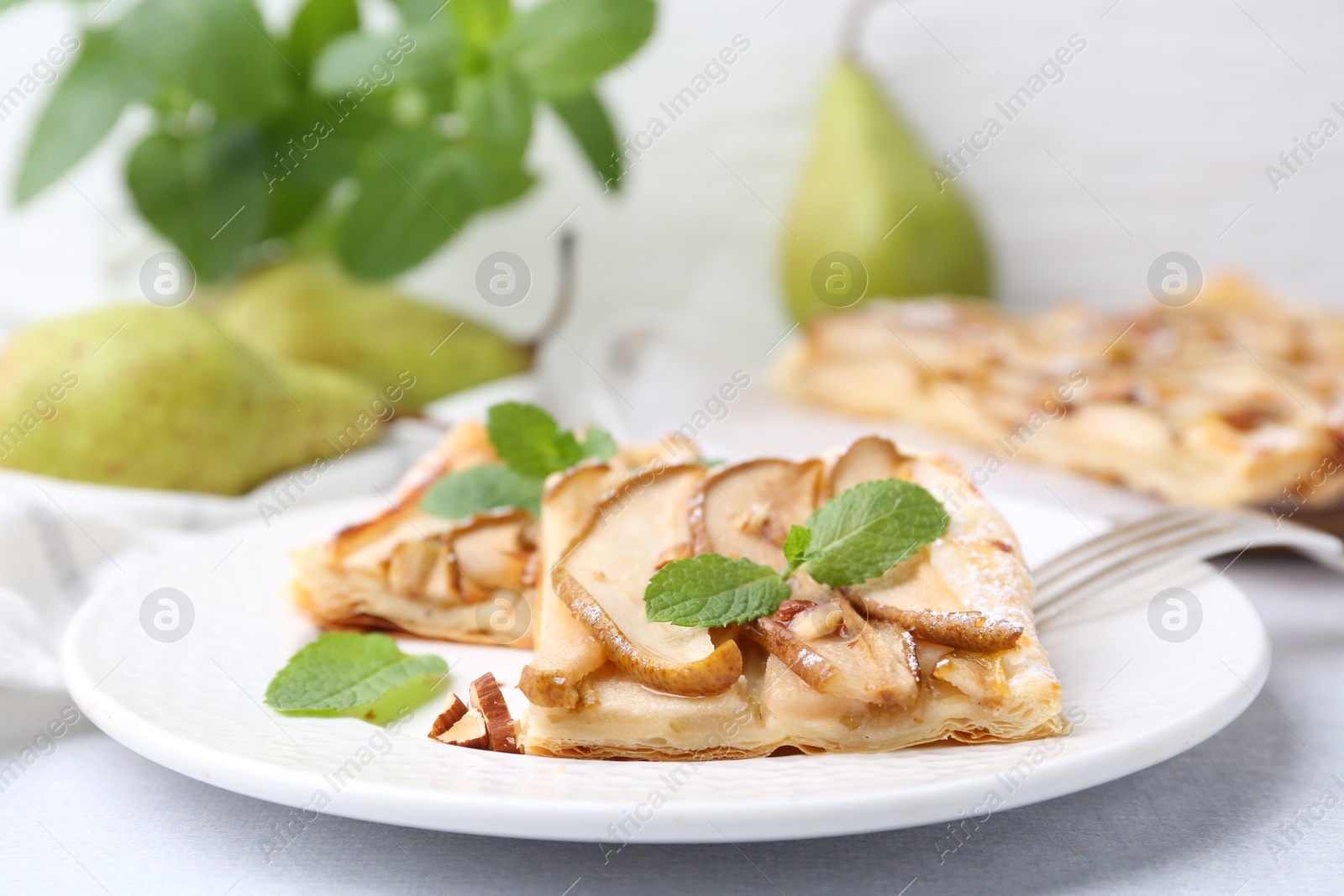 Photo of Pieces of tasty puff pastry pie with pears and mint on light grey table, closeup