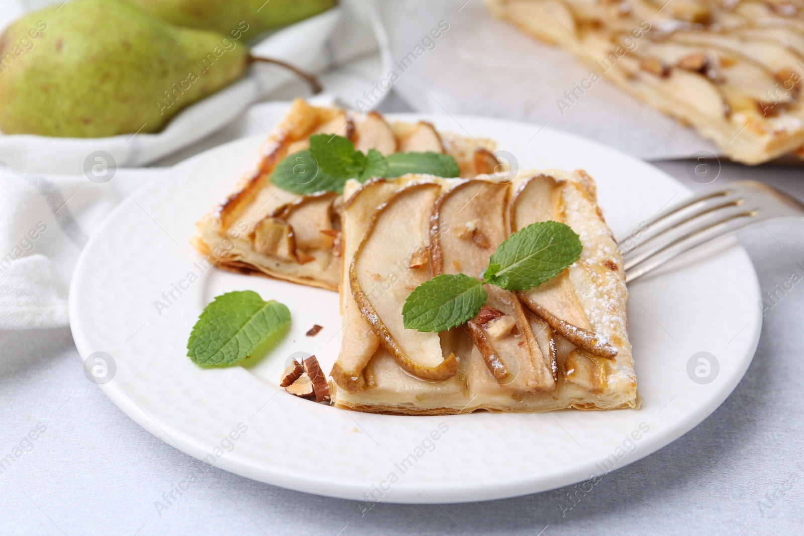 Photo of Pieces of tasty puff pastry pie with pears and mint on light grey table, closeup