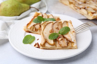 Photo of Pieces of tasty puff pastry pie with pears and mint on light grey table, closeup