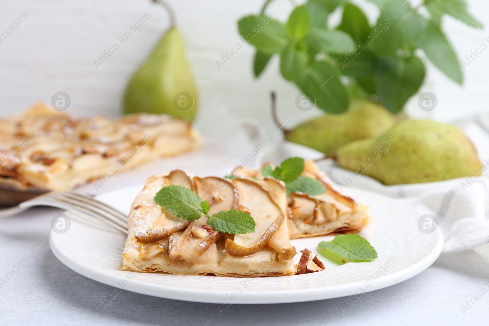 Photo of Pieces of tasty puff pastry pie with pears and mint on light grey table, closeup