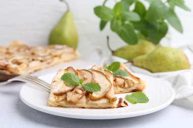 Photo of Pieces of tasty puff pastry pie with pears and mint on light grey table, closeup