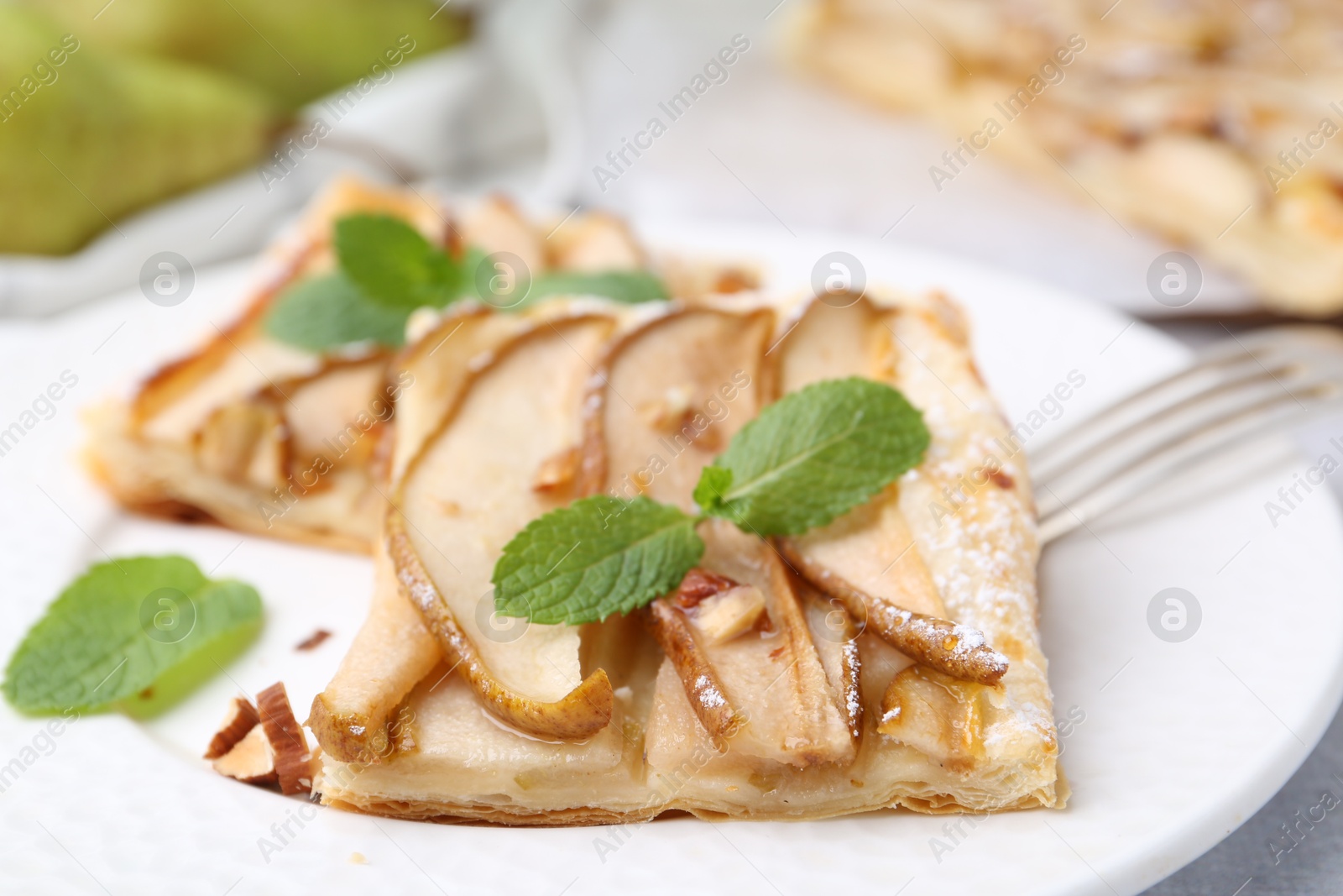 Photo of Pieces of tasty puff pastry pie with pears and mint on table, closeup