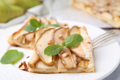 Photo of Pieces of tasty puff pastry pie with pears and mint on table, closeup