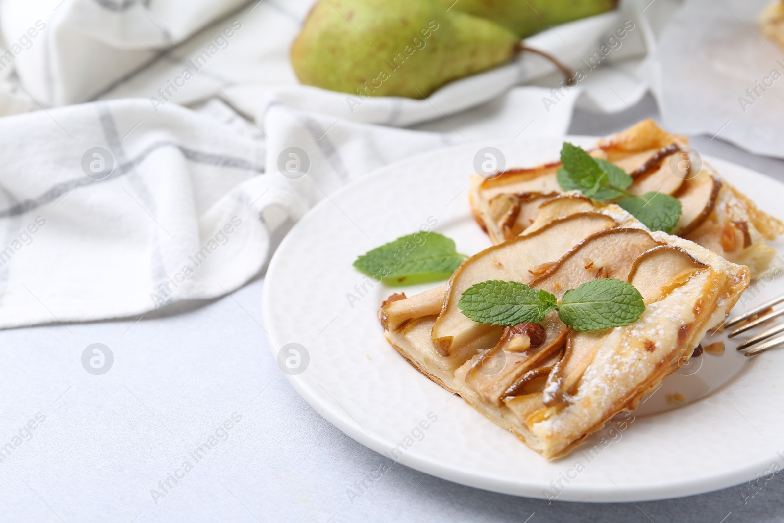 Photo of Pieces of tasty puff pastry pie with pears and mint on light grey table, closeup