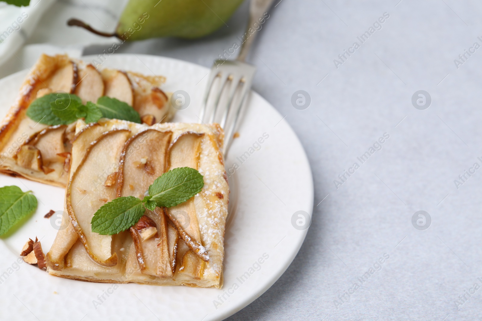 Photo of Pieces of tasty puff pastry pie with pears and mint on light grey table, closeup. Space for text