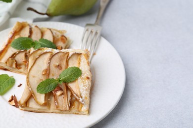 Pieces of tasty puff pastry pie with pears and mint on light grey table, closeup. Space for text