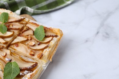 Photo of Tasty puff pastry pie with pears and mint on white marble table, closeup. Space for text