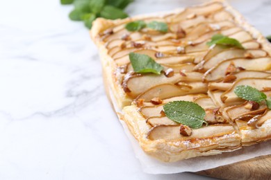 Photo of Tasty puff pastry pie with pears and mint on white marble table, closeup. Space for text